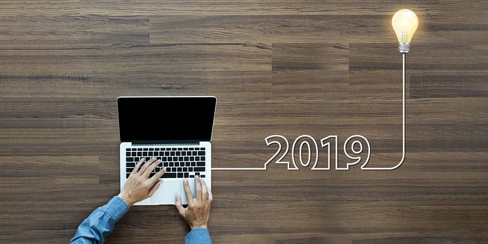 Person using a laptop on a wooden desk with "2019" and a lightbulb illustration, symbolizing new ideas or innovation for the year 2019.
