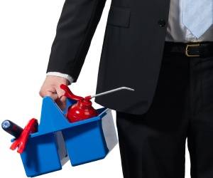 A person in a business suit holds a blue plastic caddy containing cleaning supplies, including a red oil can and other tools.