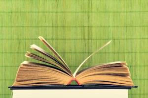An open book with pages slightly fanned out rests on top of a closed book against a green textured background.