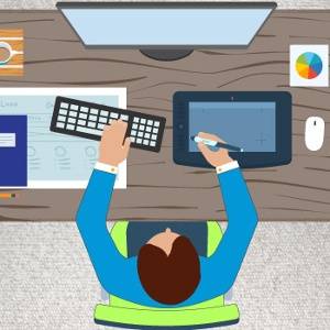Illustration of a person at a desk using a keyboard and a tablet, with a monitor, mouse, coffee cup, paperwork, and a colorful chart also on the desk.