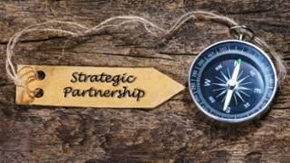 A compass and a wooden tag labeled "Strategic Partnership" rest on a rustic wooden surface, symbolizing guidance and collaboration.
