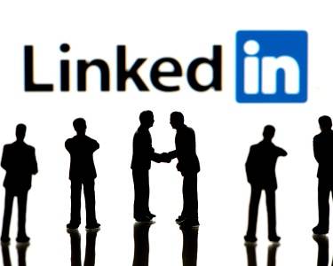 Silhouettes of people standing and shaking hands in front of a large LinkedIn logo on a white background.