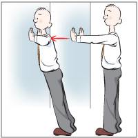 A person in business attire performs a standing wall push-up, with arms extended toward the wall and body leaning forward.