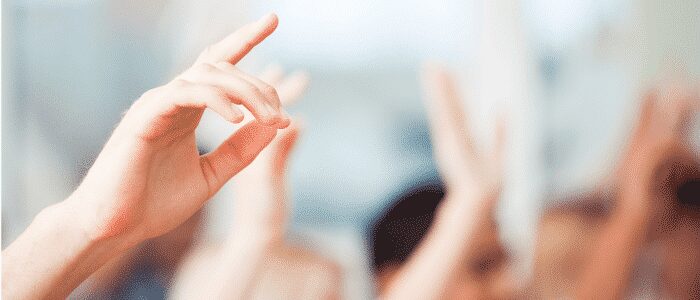 Several raised hands, with one hand in clear focus and others blurred in the background, suggesting people participating or volunteering in a group setting.