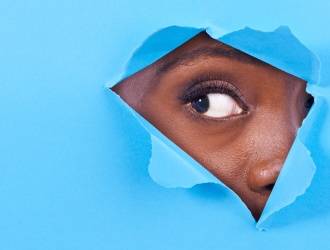 A person's eye and part of their face are visible through a triangular tear in a sheet of bright blue paper.