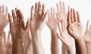 Several raised hands of diverse skin tones are shown against a plain background, suggesting participation or volunteering.