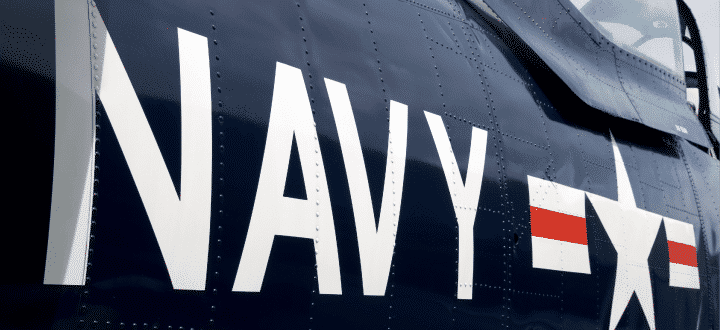 A close-up view of the side of a dark blue U.S. Navy aircraft displaying large "NAVY" lettering and a white star insignia with red and white bars.