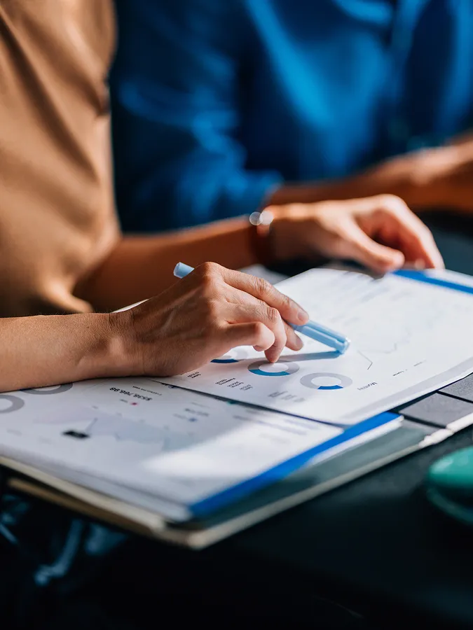 A person holds a pen and points at a paper document with charts and graphs during a meeting or discussion.