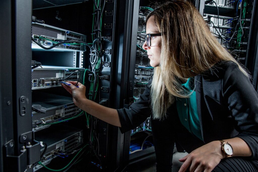 A person in business attire adjusts cables in a server rack in a data center, surrounded by network equipment and wiring.