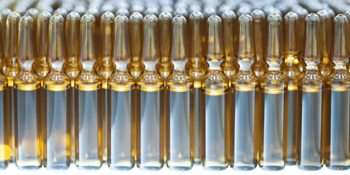Rows of transparent glass ampoules filled with liquid, arranged in a uniform pattern, viewed from the side.