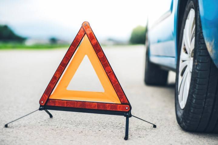 A warning triangle is placed on the road near the rear wheel of a blue car, signaling a possible roadside emergency or breakdown.
