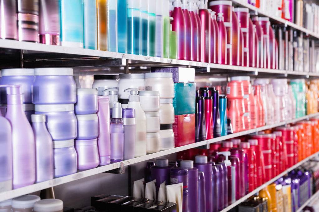 Shelves filled with various colorful bottles and containers, likely holding hair and beauty products, arranged in rows at a store.