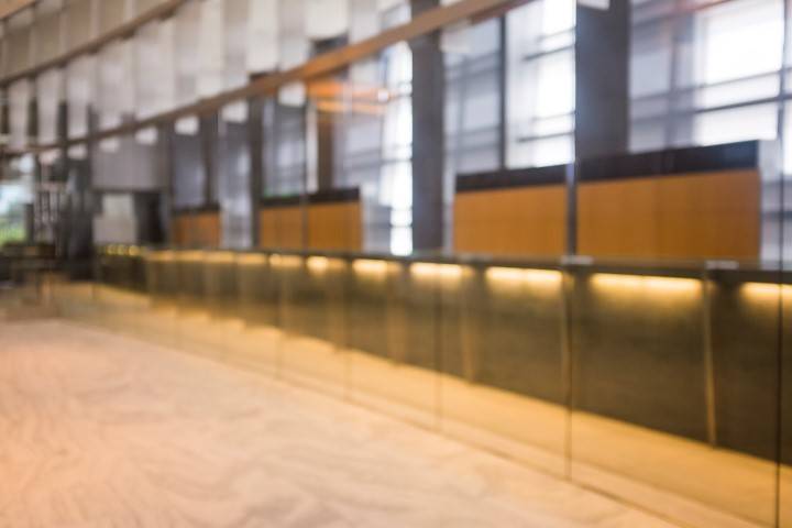 A blurred image of a modern lobby or reception area with a long counter, glass dividers, and large windows letting in natural light.